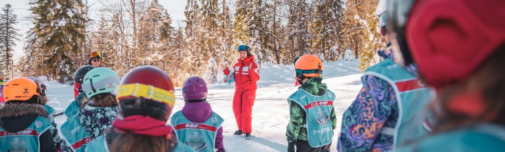 Cours de ski avec moniteur expliquant des consignes à un groupe d'enfants