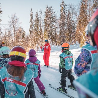 Cours de ski avec moniteur expliquant des consignes à un groupe d'enfants