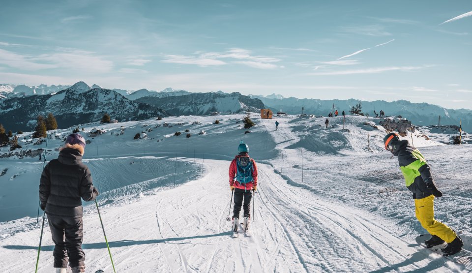 Groupe de jeunes skieurs et snowboarder qui skient avec un ciel bleu en fond